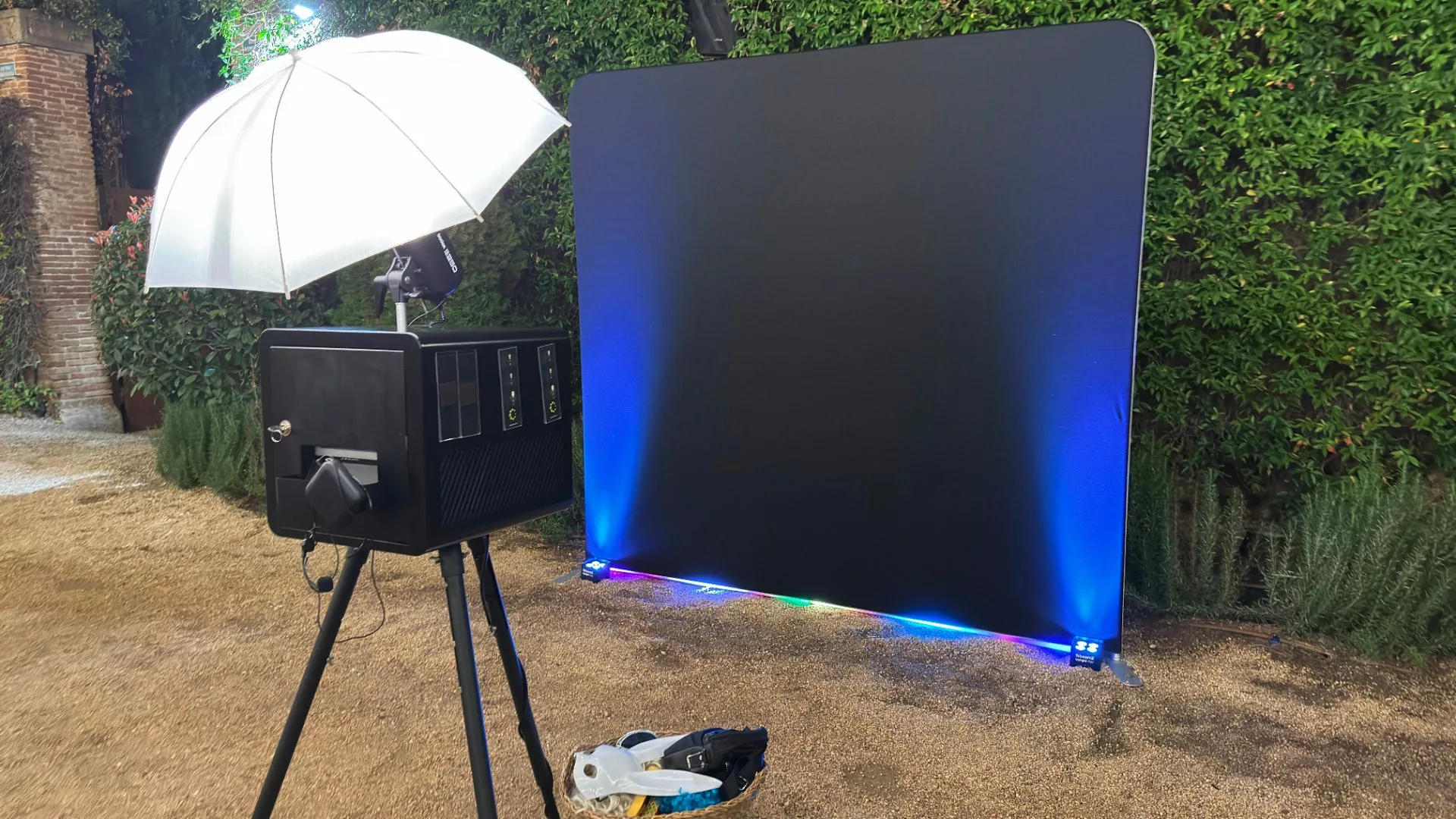 Fotomatón Modern con paraguas de luz junto a un photocall negro iluminado con luces LED azules en un evento al aire libre
