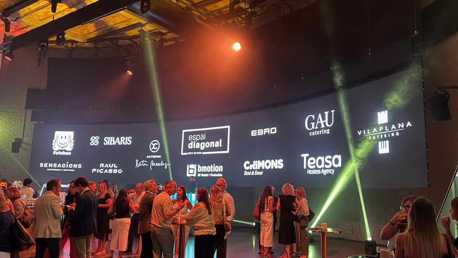 Guests at a corporate event with a backdrop showing the sponsor brands